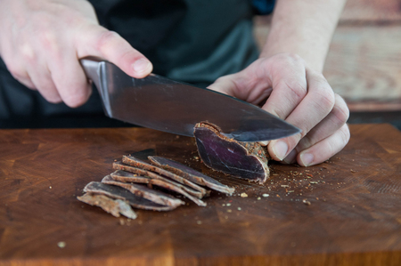 Portion of Beef Jerky cutting into slice on a cutting table with a kitchen knife on a vintage wooden backgroundの写真素材