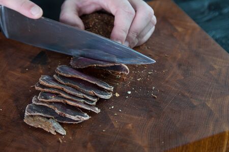 Portion of Beef Jerky cutting into slice on a cutting table with a kitchen knife on a vintage wooden backgroundの写真素材