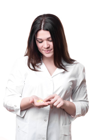 Female doctor holding medication isolated on a white background. She looks at the pills and smilingの写真素材