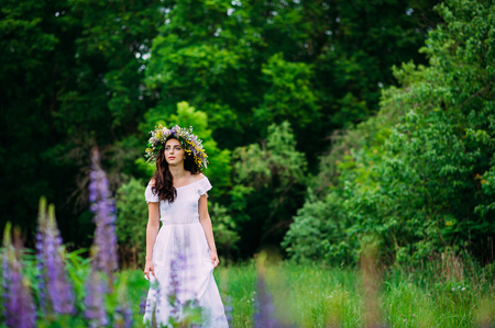 Beauty Girl Outdoors enjoying nature.Girl with a wreath of wildflowers on her head walks along the path.の写真素材