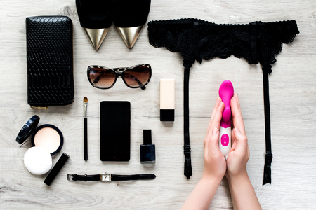 Top view of female fashion accessories for woman. Sex toy in the hands, sunglasses, face powder, make up brush, nail polish, watch, mobile phone, lipstick, gold pointed shoes, purseの写真素材