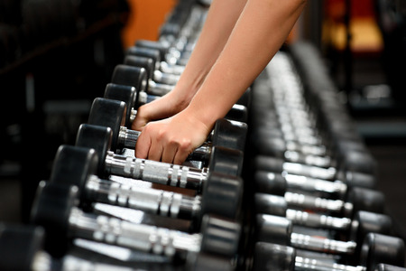 female hands close up taking dumbbells from row of barbells in a gym