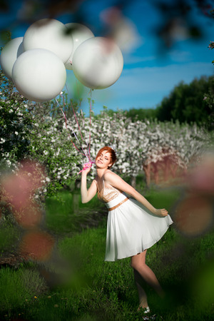 Cute cheerful female having fun with bunch of white balloons in spring garden, birthday celebration, happiness conceptの写真素材
