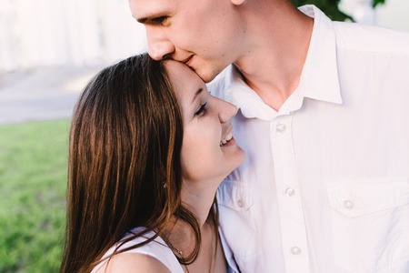 Glad guy kissing his laughing girls forehead gently. The boyfriend kisses the girlの写真素材