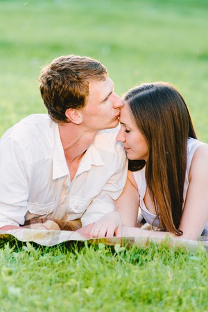 Man kissing his girl's forehead, eyes closed, green background. Boyfriend kissing his girlfriendの写真素材