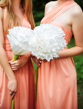 Two girls in pink dresses holding huge paper white flowers smiling. Bridesmaidsの写真素材