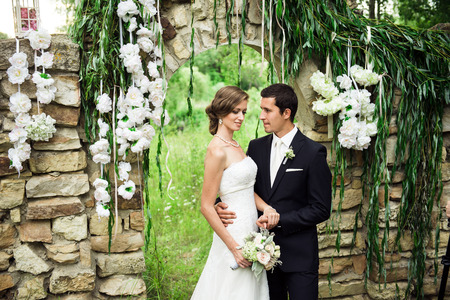 Wedding couple cuddling at the outside wedding ceremony on the nature , stone arch and white flowers on their backgroundの写真素材