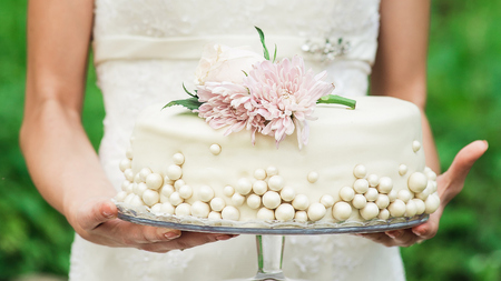 The bride holds a wedding cake. A wonderful cake with white decorations in gentle female handsの写真素材