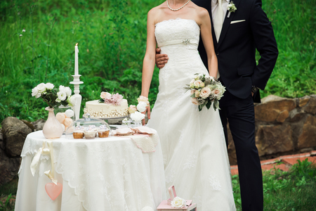 Newlyweds cuddling near the cute table with sweets, greenery behind themの写真素材