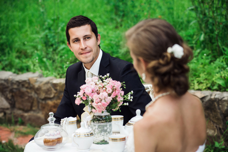 Young groom looking delighted at his bride as they sit at the table having tea togetherの写真素材