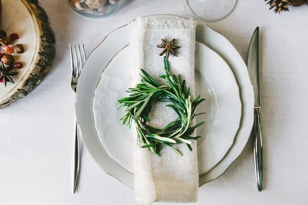 Decorative green wreath on a napkin as a part of table appointments, clean white tablecloth background, top view. Christmas table place setting.の写真素材