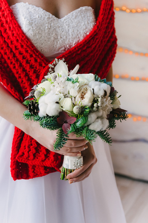 Bride in a white dress and red scarf with a white bouquet in her hands, winter weddingの写真素材
