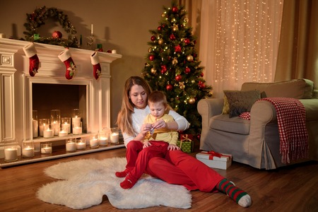 Young mom with her son on her knees sitting on a furry carpet and opening a chocolate sweet for himの写真素材