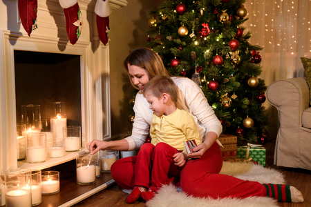 Young mother and her son lighting white candles on a christmas decorated fireplace. Christmas Room Interior Design. Copyspaceの写真素材