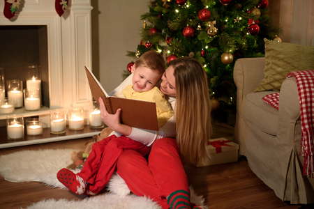 Family of a boy and his mom are reading a nice book laughing together, cozily decorated christmas room. Happy family reading together on Christmas evening.Winter evening at home for parents and kidsの写真素材