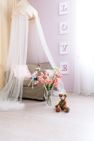 View of room design for girl. A gently pink colored room, a comfortable armchair with a canopy above it, pink flowers and a lovely doll, huge love letters on the wallの写真素材