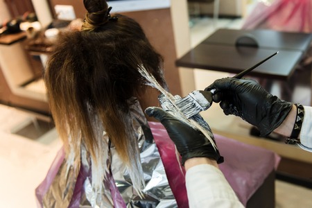 Professional hairdresser coloring hair. A close picture of a dying hair process, a man working with a wet hairbrushの写真素材