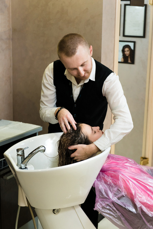 Portrait of young female client having her hair washed in beauty salon. A hair master washing a girl's hair gently in a high tech sinkの写真素材