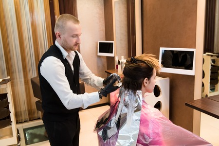 Professional male hairdresser choose hair dye color at modern salon, female customer change hair color. A male hair master dying his client's fair hair in the salonの写真素材