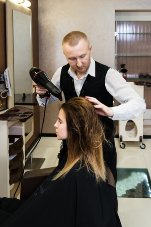 Professional hairdresser drying hair. A photo of a neat hairdresser working at a girl's hair with a hairdryerの写真素材