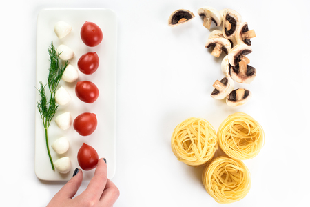 Upper view on fresh vegetables and spaghetti on isolated in white, a female hand touching a red tomato, pasta, greens, mushrooms. Top view with, copy space. Healthy food backgroundの写真素材