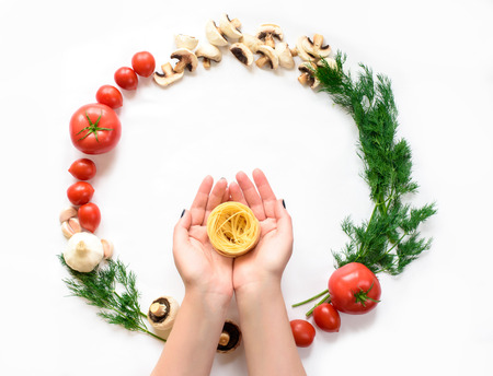 Top view of Female hands holding a pasta, a range of vegetables. A colorful circle of a pasta ingredients on a white backgroundの写真素材