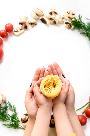 Italian pasta and sauce held in hands, red white and green contrast. Top view of female and child hands holding a pasta, a range of vegetablesの写真素材