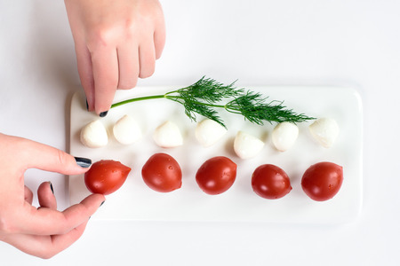 Gentle female hands fixing a composition of an upper view on a tomato and cheese composition isolated in white. Top view with copy space. Healthy food background with various vegetables ingredientsの写真素材