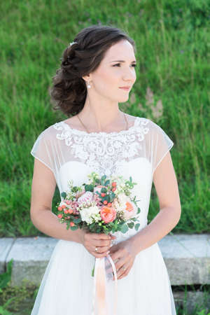Portrait young beautiful bride in a white wedding dress looking aside, fresh green summer grass on her backgroundの写真素材