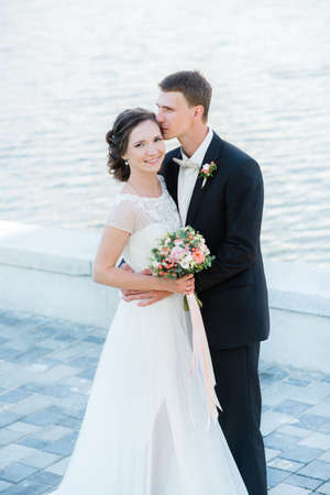 Happy young couple just married. ? lassic wedding picture of a bride and groom's huggs near the waterの写真素材
