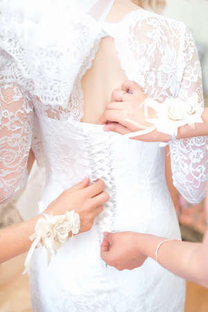 Bridesmaid preparing bride for the wedding day, helping fasten her dress. Closeup bride is getting...