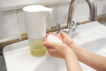 Automatic dispenser of liquid soap in the bathroom close-up. A little boy washes his hands. The concept of hand washing, hygiene. Coronavirus concept. Pandemic protection. Preventionの写真素材