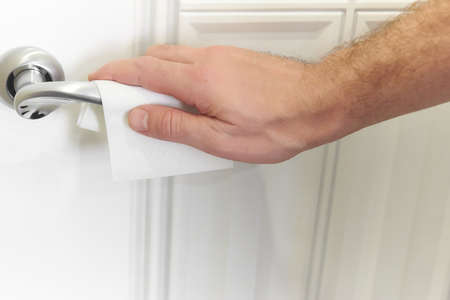Man hand cleaning desinfected metallic door handle door knob with the paper tissue against the virus