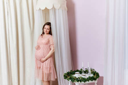 Happy pregnant woman. Portrait of a relaxed, satisfied pregnant woman in stylish and cute decor of newborn baby roomの写真素材