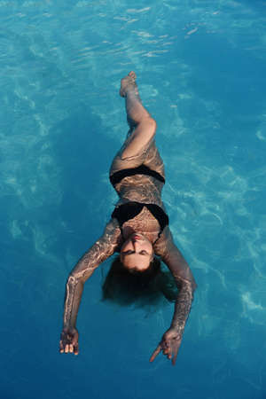 Beautiful girl relaxes in the swimming pool in sunny day. Top view of young woman in swimming poolの写真素材