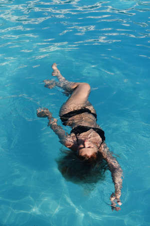 Beautiful young woman is relaxing in the spa pool, taking care of herself. Floating body concept, treatment for back. Calmness concept.の写真素材