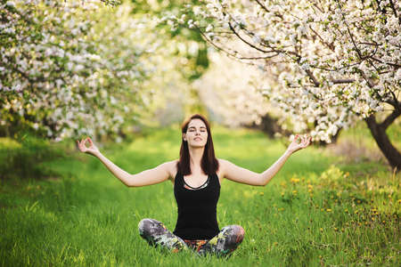 Yogi girl sitting on the green lawn raising hands up meditating in Padmasana exercise? Harmony conceptの写真素材