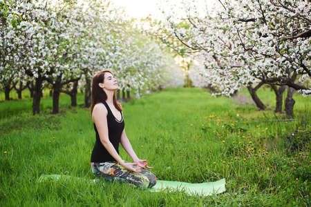 Young caucasian yogi woman with meditating seated during morning exersize on the green lawn in blooming garden, practicing breathing yoga in Virasana, outdoors meditation reduces physical fatigueの写真素材