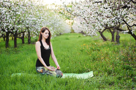 Young caucasian yogi woman with meditating seated during morning exersize on the green lawn in blooming garden, practicing breathing yoga in Virasana, outdoors meditation reduces physical fatigueの写真素材