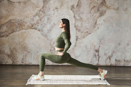 Young woman with long dark hair, wearing sportswear, doing squat exercises working on lower body legs and butt muscles create perfect body shape, side view, doing morning yoga exercise on a natural matの写真素材