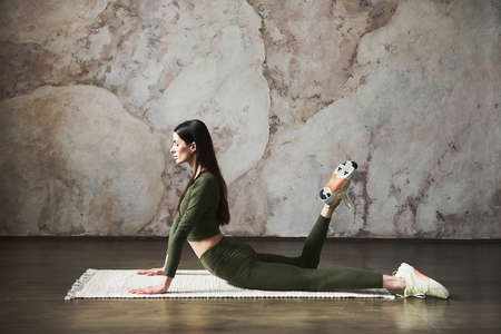 Young attractive woman with long dark hair wearing sportswear, start her day working out in yoga studio near wall, full length. Healthy lifestyle concept. Concept of flexibility for joints. Copy spaceの写真素材