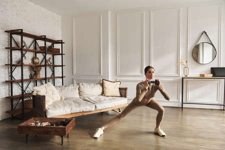Young woman doing side lunges exercise with dumbbells weight for flexibility and strength in living room. Indoor, full length, front view, copy space. Sport and body care, fitness at home concept.の写真素材