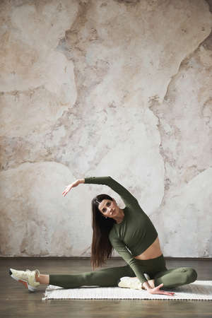 Attractive young woman doing stretching exercise at home, working out in yoga studio. Practicing yoga, working out indoor full length. Concept of flexibility for joints and ligaments.Advertising spaceの写真素材