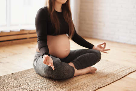 Meditating on maternity. Close-up of pregnant woman meditating while sitting in lotus position. Prenatal meditation, Pregnancy Yoga, Fitness concept, Motherhood, Pregnant woman practicing yogaの写真素材