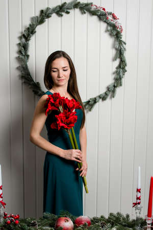 A picture of a gentle young girl with a red bouquet and a Christmas wreath behind her. Christmas room interior design.の写真素材