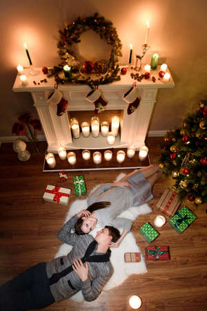 Top view of young couple laying on floor for Christmas eve, she is glancing smiling brightly for a camera. Top view of happy couple laying on floor for Christmas eve.の写真素材