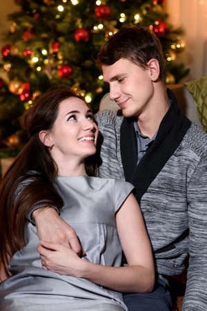 A beautiful couple hugging and looking happily at each other, christmas eve together. Couple cuddling and laughing on sofa.の写真素材