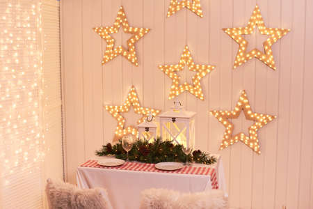 Dining room decorated for Christmas. Table with chairs set, waiting for guests. The wall is decorated with luminous stars, Xmas Home Interior. Traditionally decorated christmas tableの写真素材