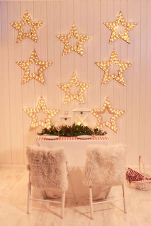 Dining room decorated for Christmas. Table with chairs set, waiting for guests. The wall is decorated with luminous stars, Xmas Home Interior. Beautiful New Year decorated classic home interior, winterの写真素材