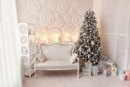 Living room interior with white sofa decorated chic Christmas tree, gifts, pillows. Xmas interior with fur-tree decoration, white wall. Christmas decorated interior with presents and New year tree.の写真素材